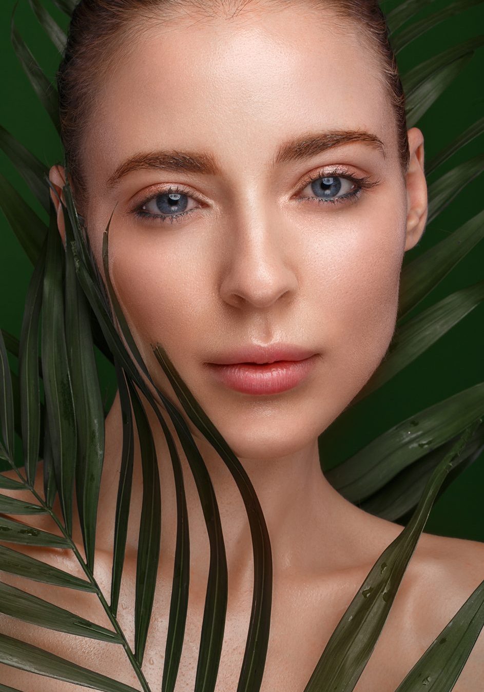 Beautiful fresh girl with perfect skin, natural make-up and green leaves. Beauty face. Photo taken in the studio.